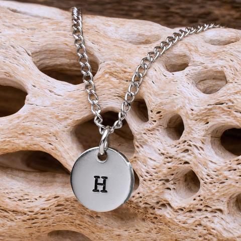 A silver medallion with a black H hanging on a silver chain 