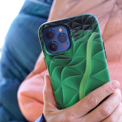 A hand holds an iPhone with the Presidio Edition: Thermal Green Collection case on it in front of a quilted blanket