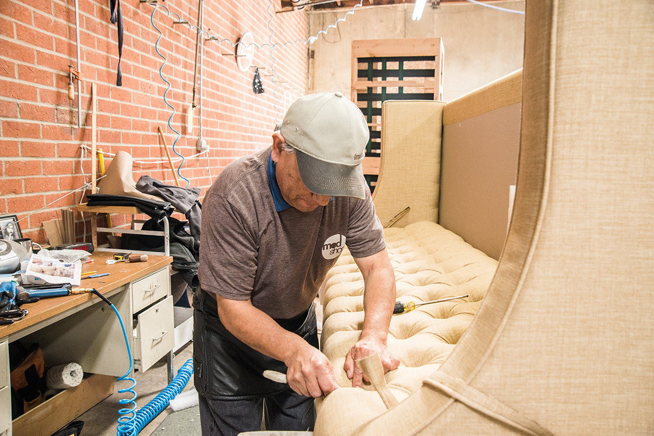 Close-up of furniture factory worker bending over cream-colored furniture cushion, working on upholstery with a hand tool