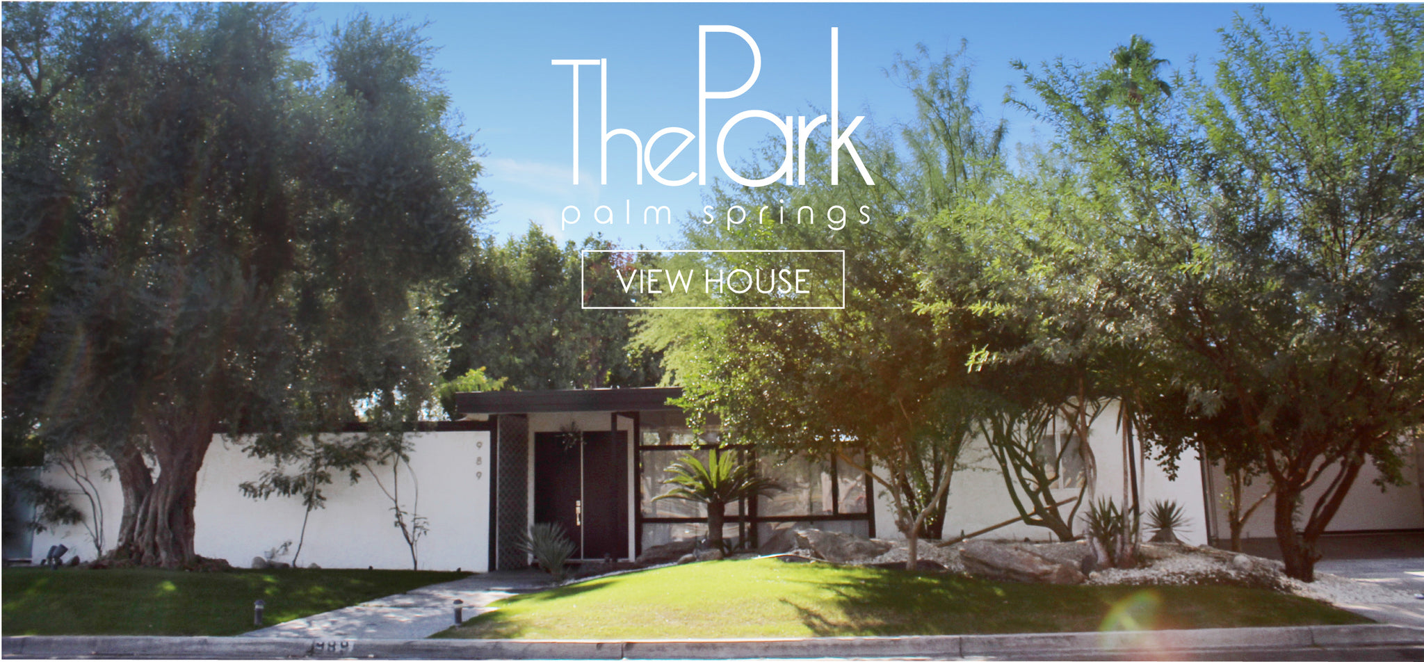 Front of one-story white house with dark trim and trees. 'The Park Palm Springs' and 'View the House' in white print overlay