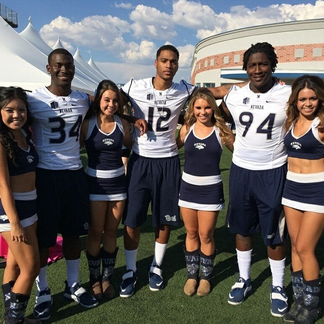 UNR cheerleaders posing with football players. The girls are wearing UNR cowboy boot covers over their cowgirl boots