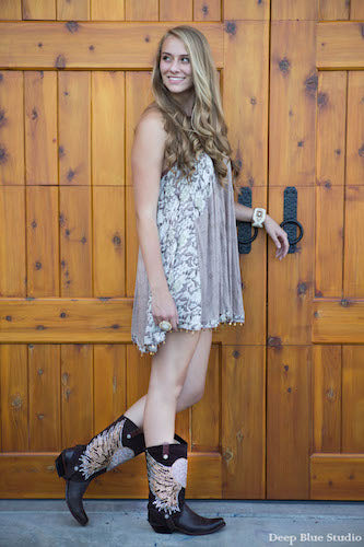 blonde woman wearing a white floral dress with brown cowboy boots with brown cowgirl boot covers with a heart design