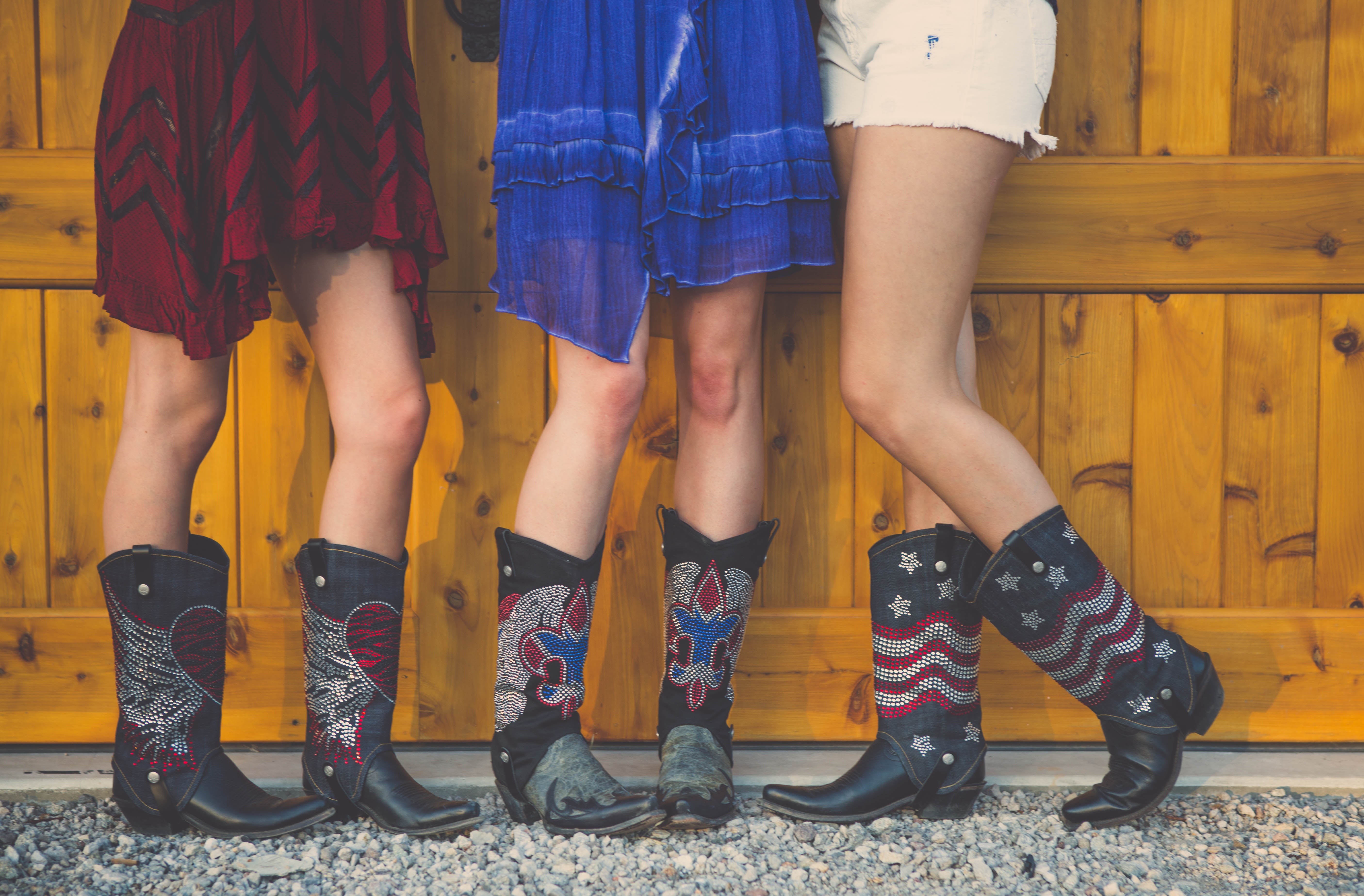 three women smiling, wearing dresses and cowgirl boots with cowboy boot covers