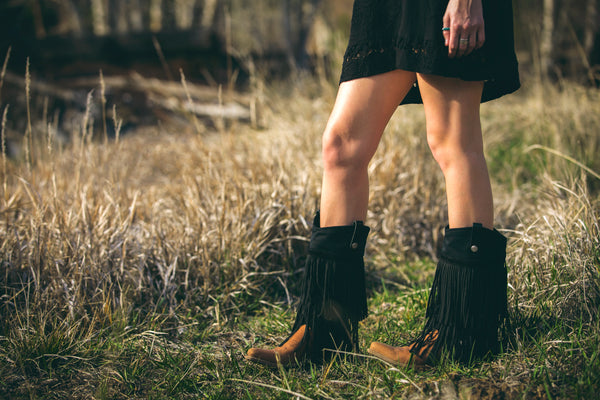 girl in a field wearing black fringe cowgirl boots
