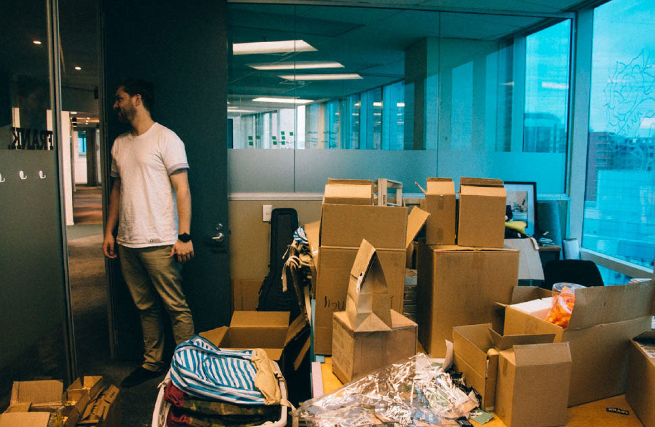 Image of Jason standing in the office with lots of boxes around. Getting ready to give away stationery to children in need.