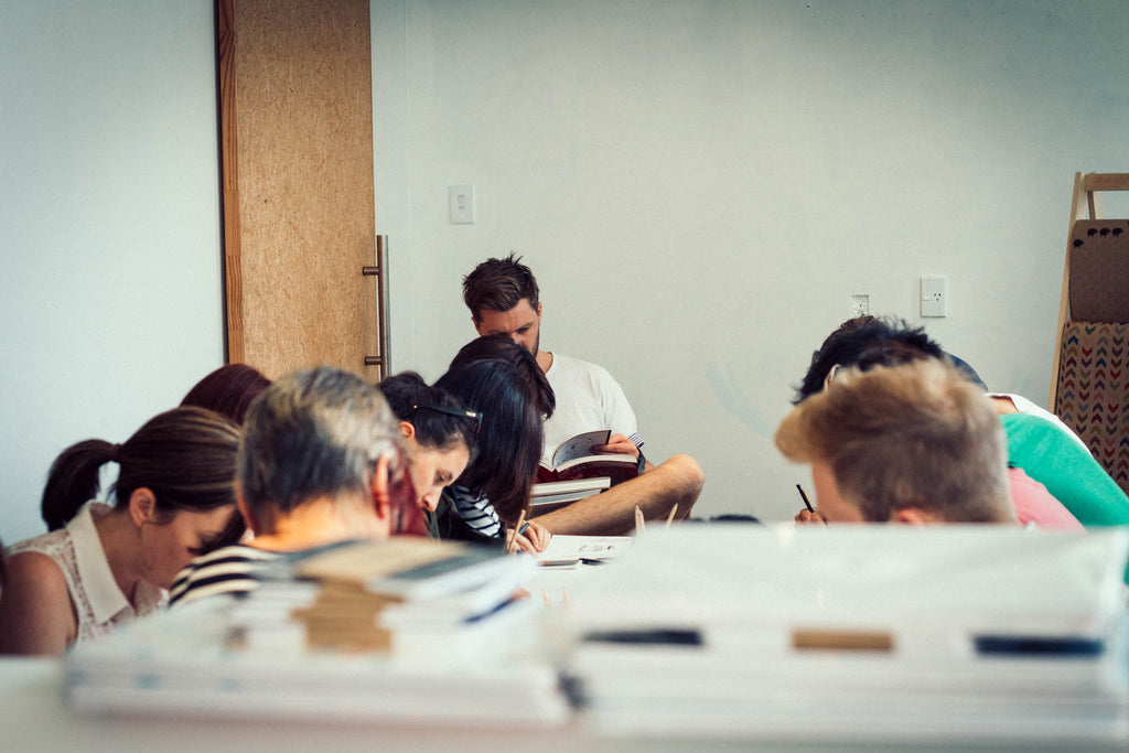 Image of the whole group drawing and illustrating at a small desk in The Market Pop Up store