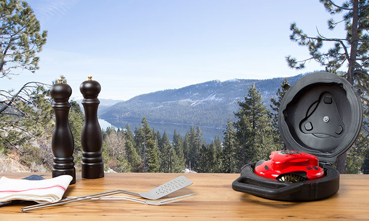 Red Automatic Grill Cleaner Robot in Black Grillbot Carrying Case with Mountains in the Background