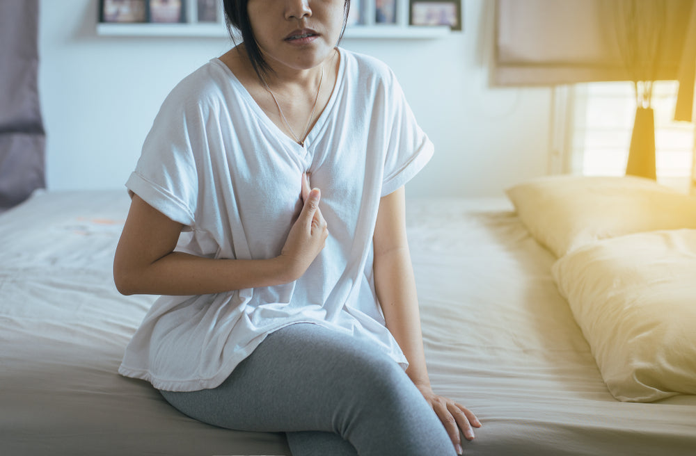 woman on bed holding chest from heartburn