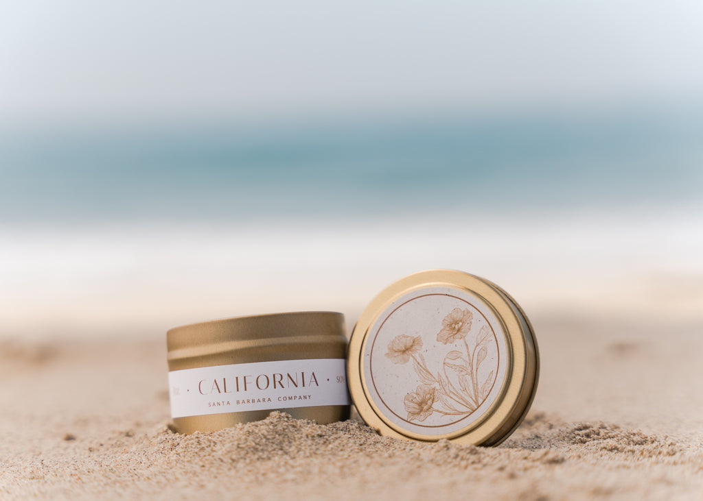 California candle in gold tin on sand oceanside
