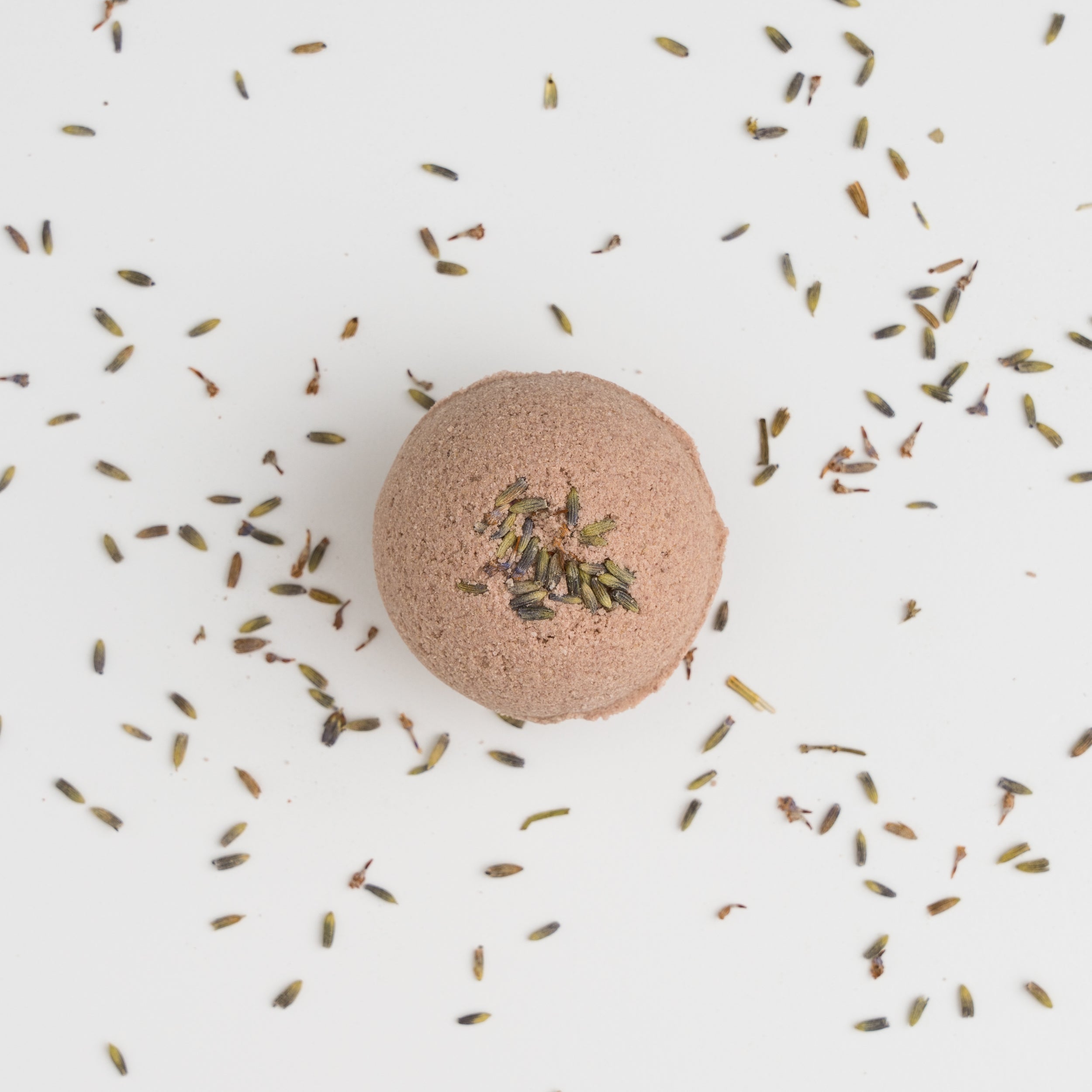 Light purple bath bomb with dried lavender sprinkled around it on a white background