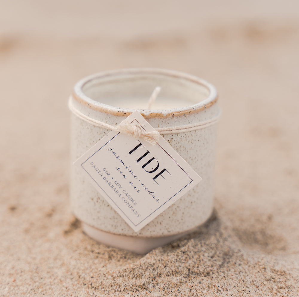 Small white ceramic candle sitting in sand with a tag tied around it.