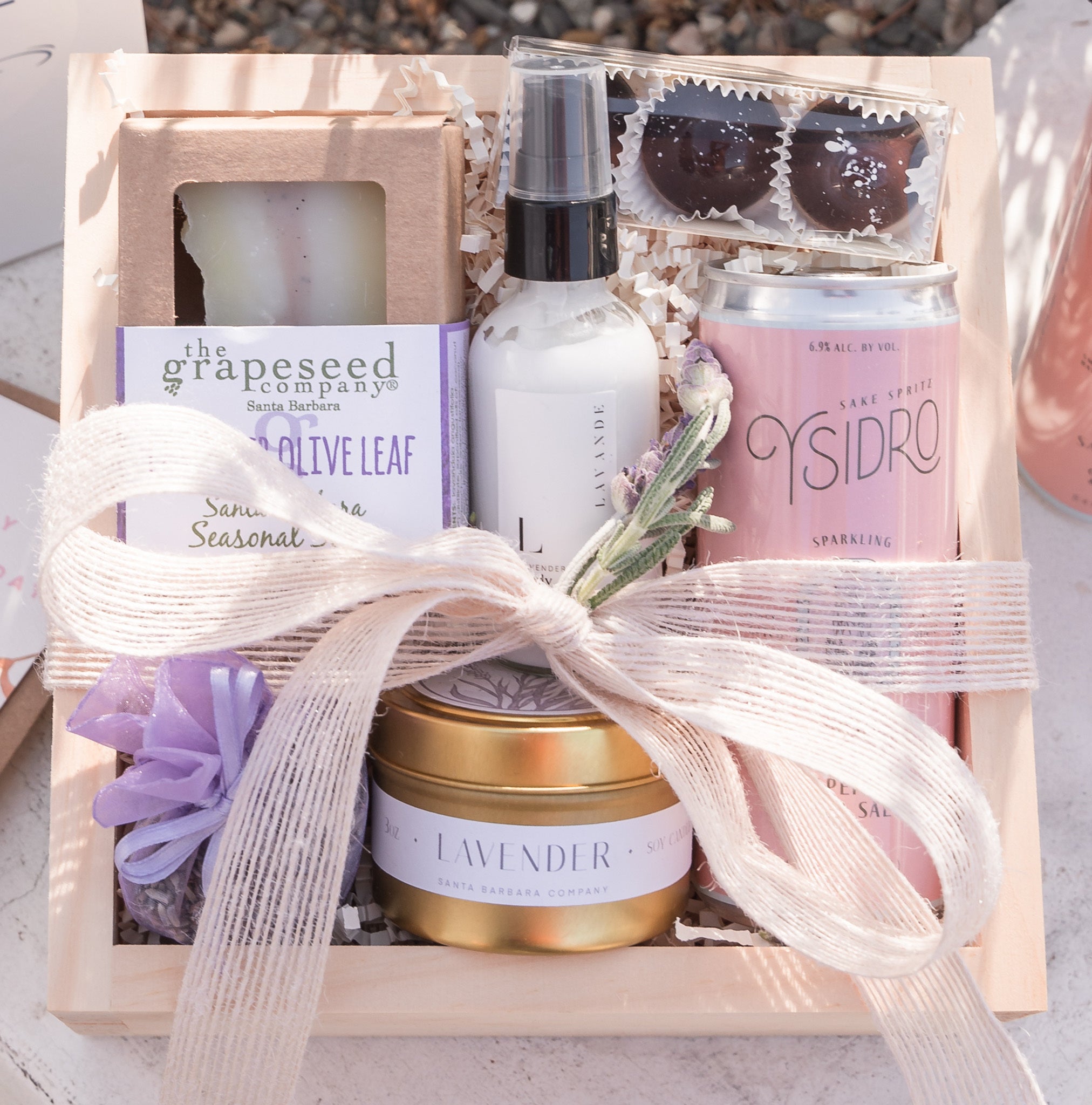 Pink and purple themed wood box with soap, lotion, truffles, candle, lavender sachet, and a can of sake