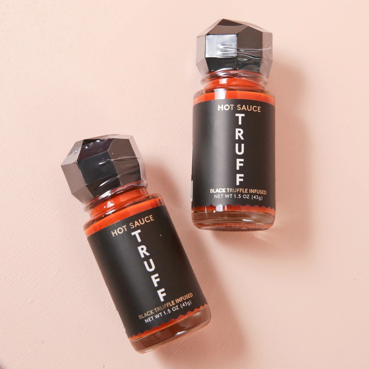A mini bottle of Truff Hot Sauce in a glass bottle with a black label and black geo shaped lid.