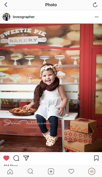Toddler sitting on a bench in front of bakery with an Everything Dawn Bakery Candles fake cherry pie