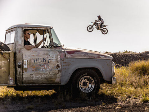 Man jumping motorbike over old car