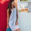 Woman in dress leaning against wall and smiling.