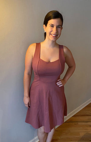Front image of Heather in front of a grey wall wearing a pink A-line dress with wide straps