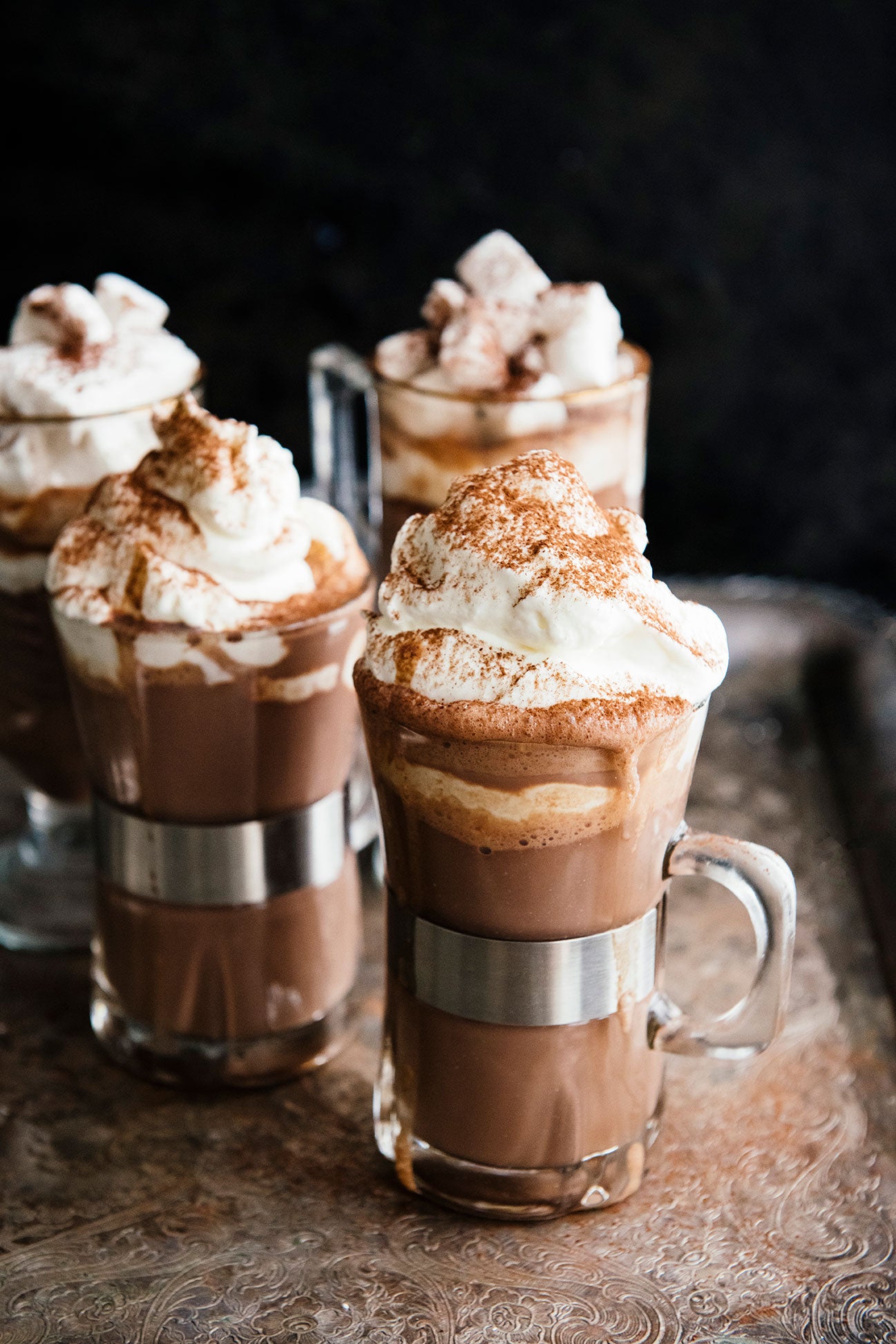 Glass mugs of hot cocoa with square marshmallows and soft scoops of whipped cream.