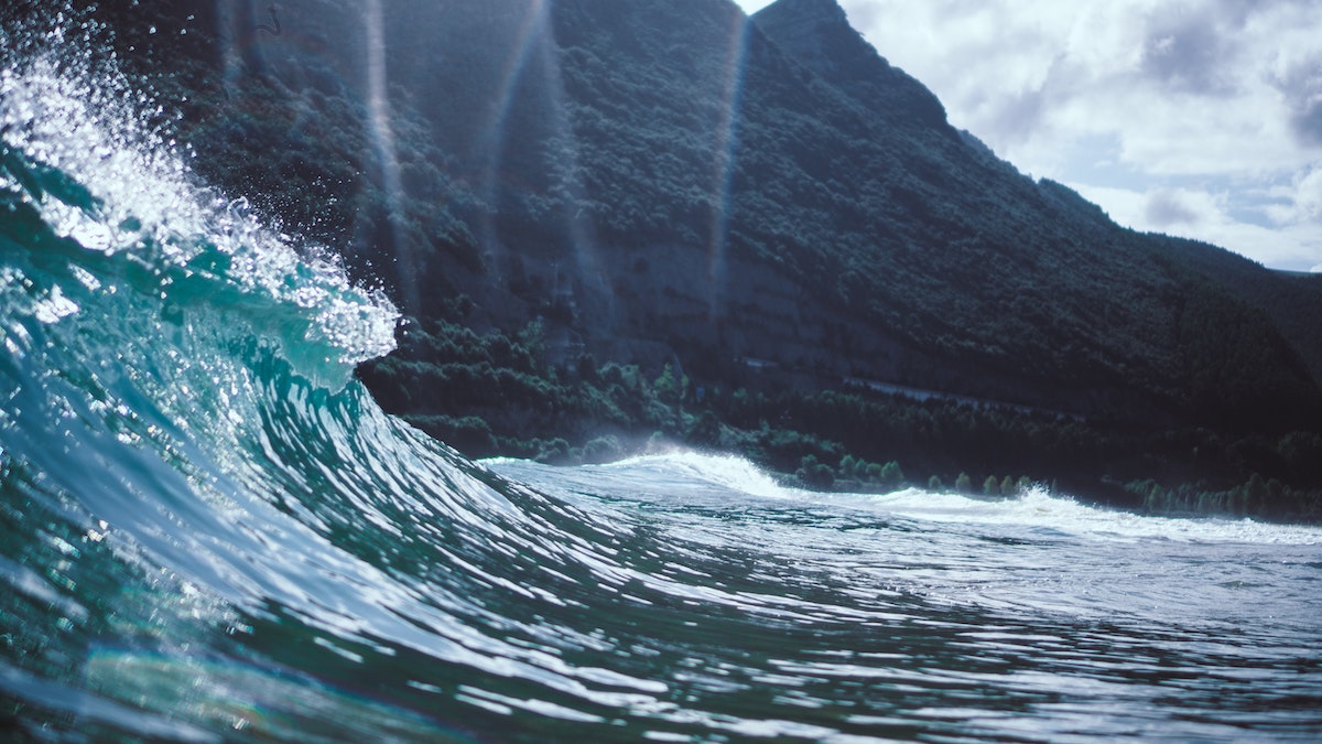 a wave starting to crest with mountains in the background