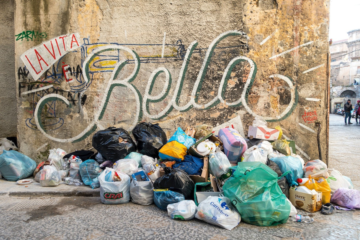 plastic bags full of garbage on a street corner with street art behind it