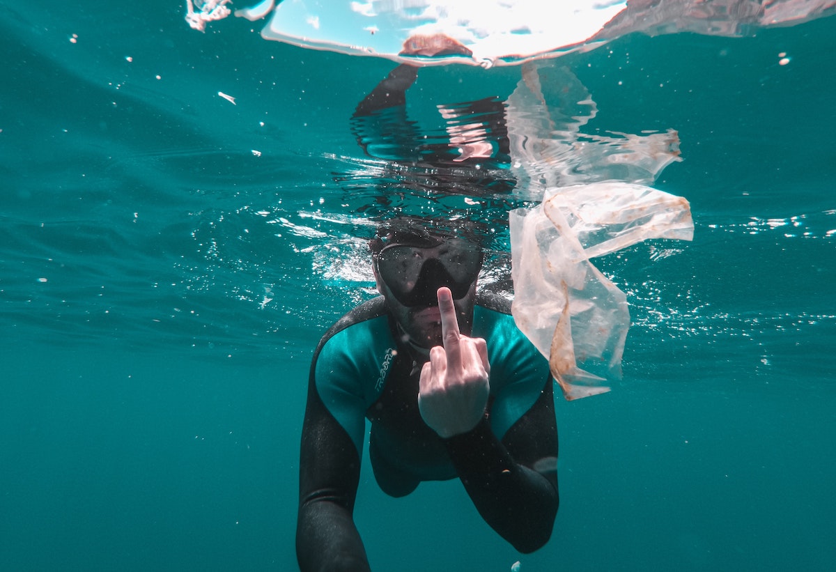 snorkler in the ocean giving the middle finger to camera while a plastic bag floats in front of him