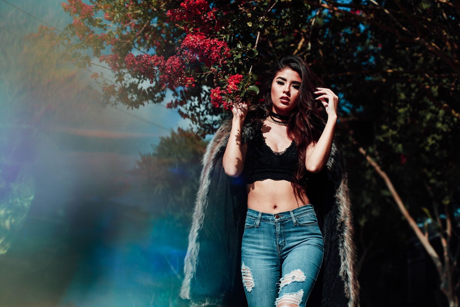 woman in black top, jeans, and faux fur coat around flowers