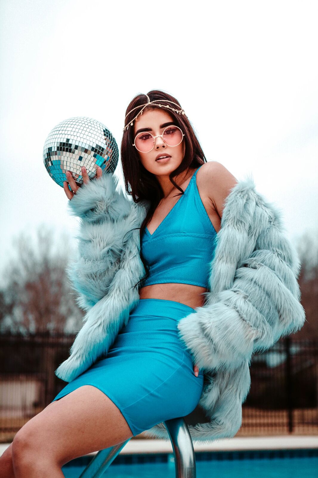 woman in blue outfit and faux fur coat holding disco ball