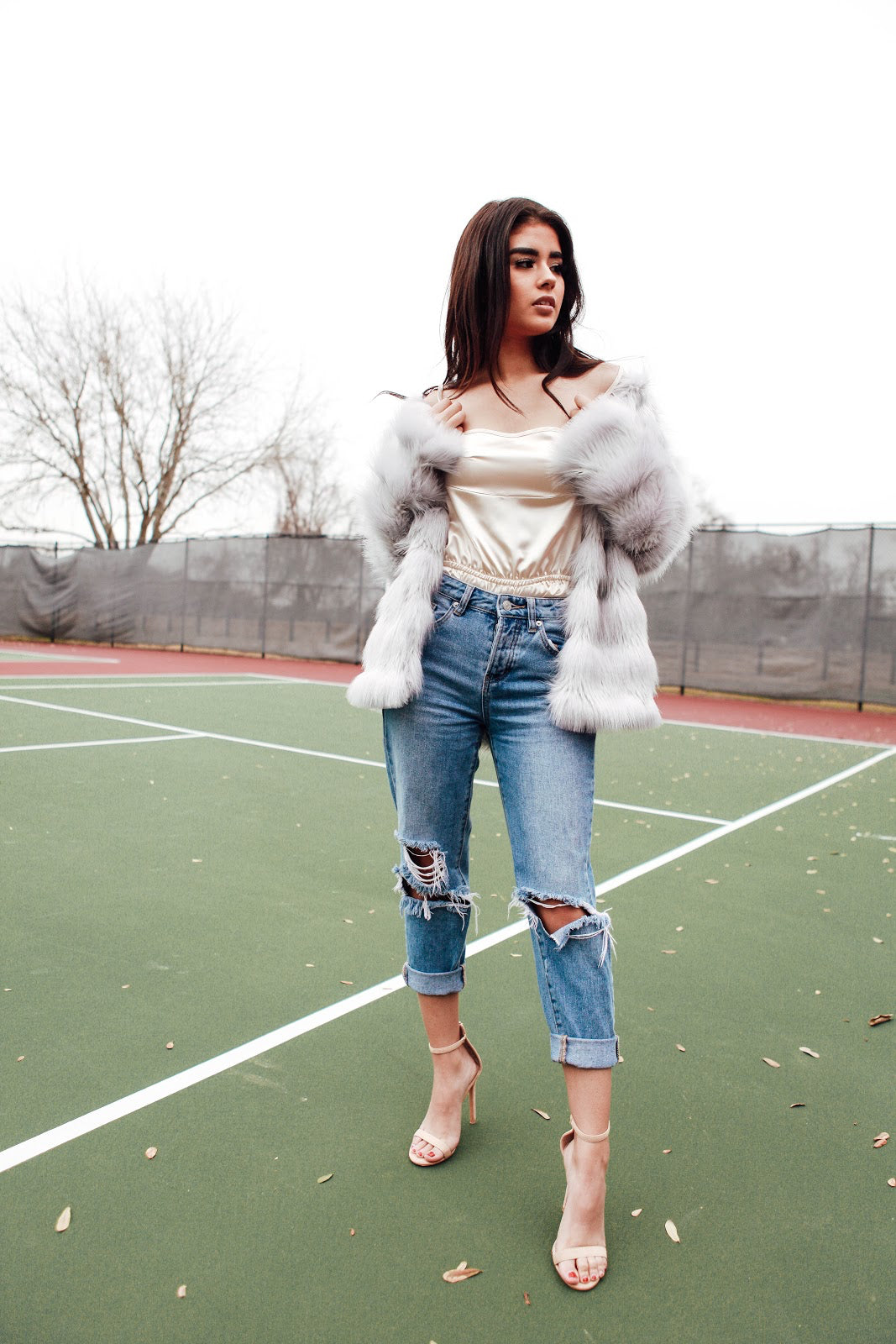 woman wearing satin top, heels, jeans, and faux fur coat