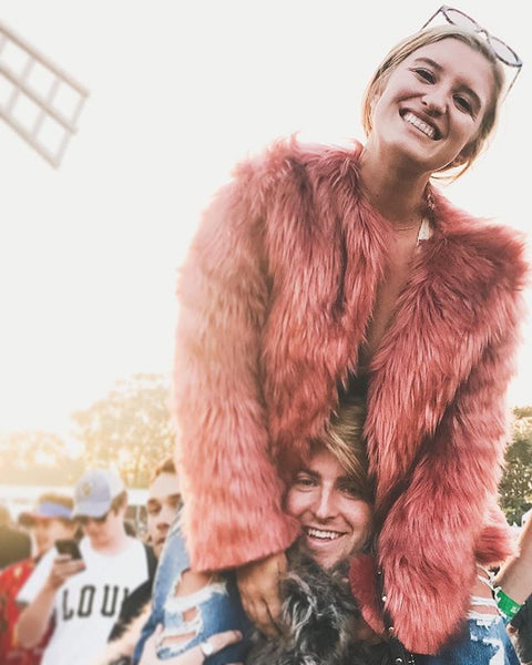 woman with glasses on head sitting on shoulders of man while wearing faux fur coat