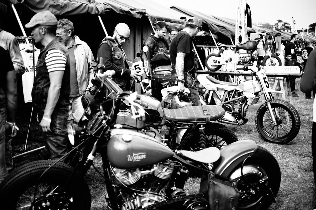 Stylish motorcyclists watch custom motorcycles at tents at Wheels and Waves village