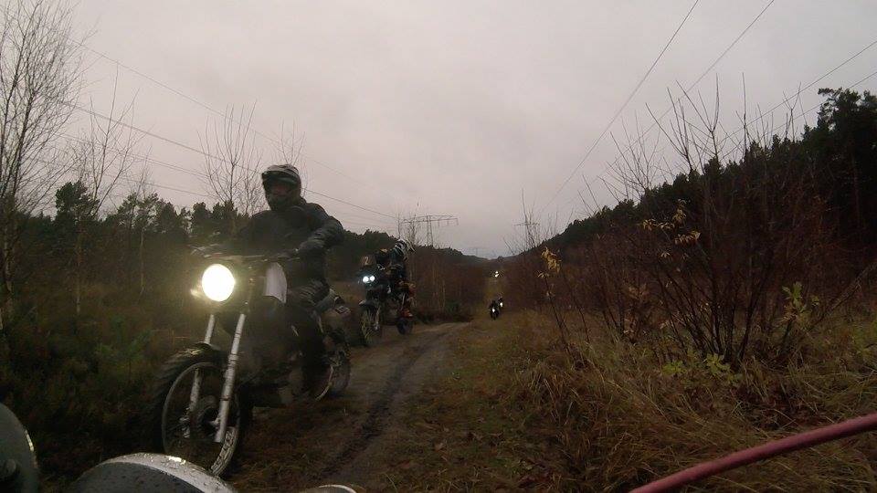 Riders in motorcycle waterproof gear riding dirt road in dim light and rain