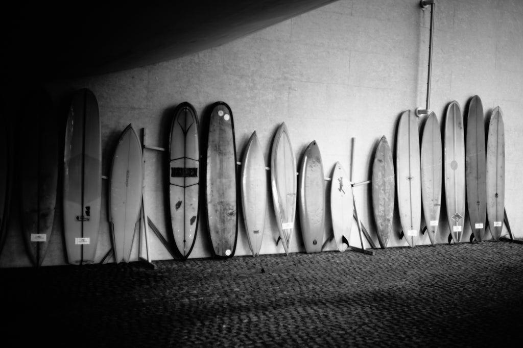 15 different surfboards leaning against a wall at Wheels and Waves Festival