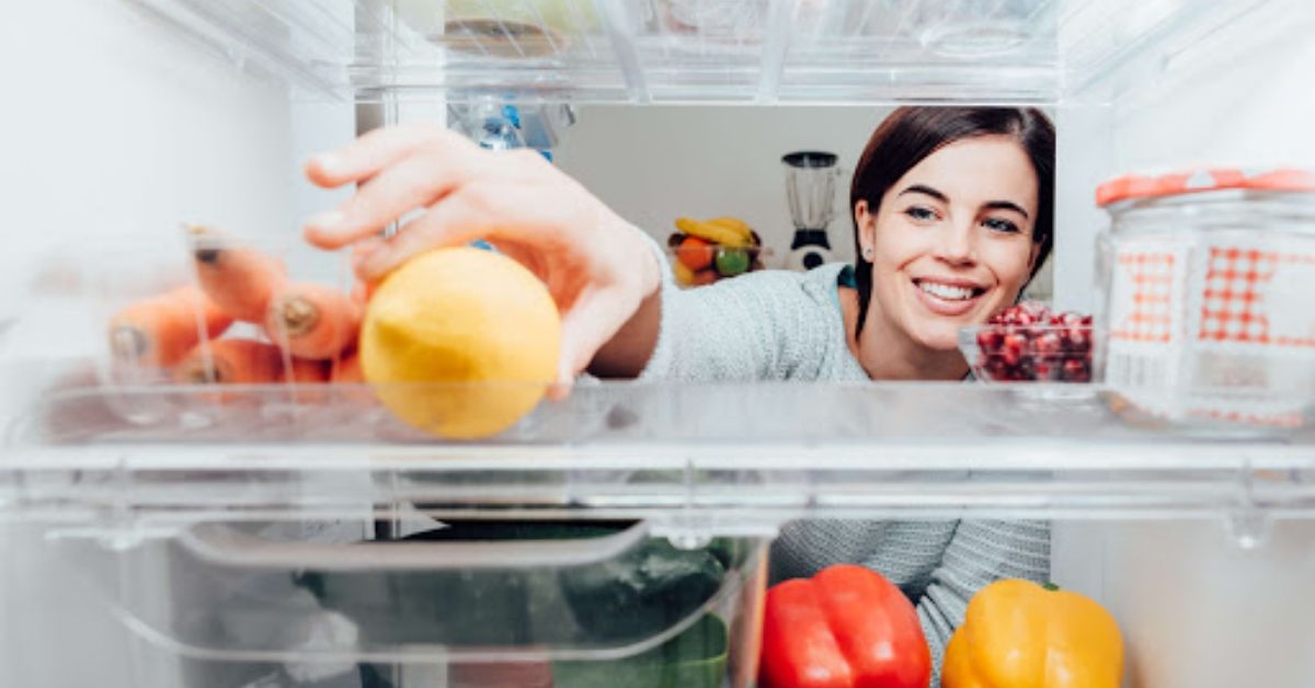 A woman looking inside the refrigerator and reaching for a lemon.
