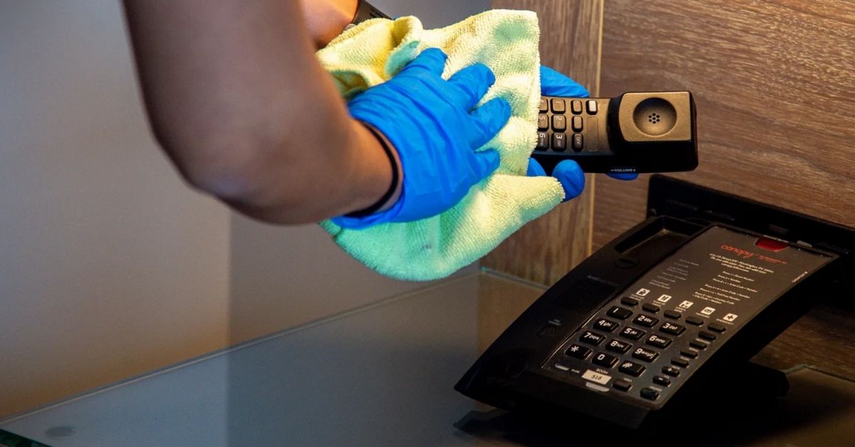 Someone wiping down a phone while wearing gloves.