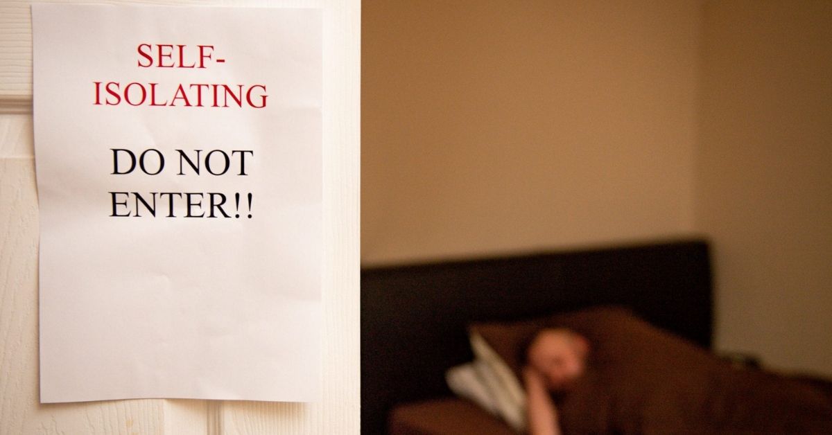 A sign on the door reads Do Not Enter, Self Isolating. There is a person sleeping in the background.