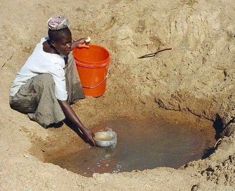 boy scooping water in soil hole
