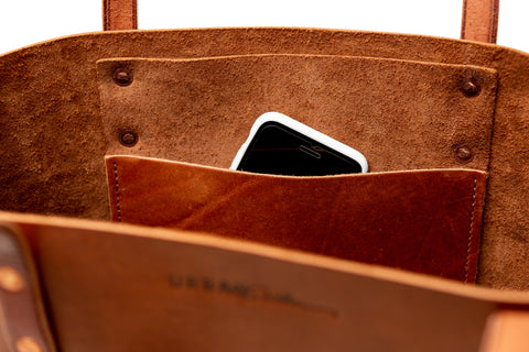 Close up of opening of a leather tote bag showing an interior pocket with a cell phone peeking out