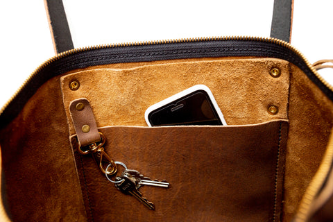 close up of interior of mocha leather tote showing pocket & key fob with cell phone peeking out