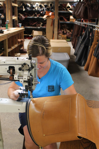 same woman sits at industrial sewing machine making a leather tote bag
