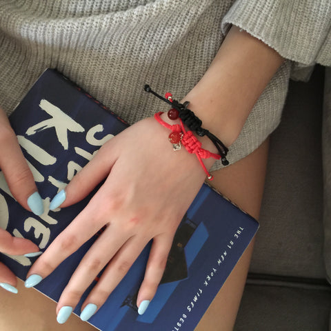 Friendship Bracelet - String of Destiny in Red and Black on lap with a book