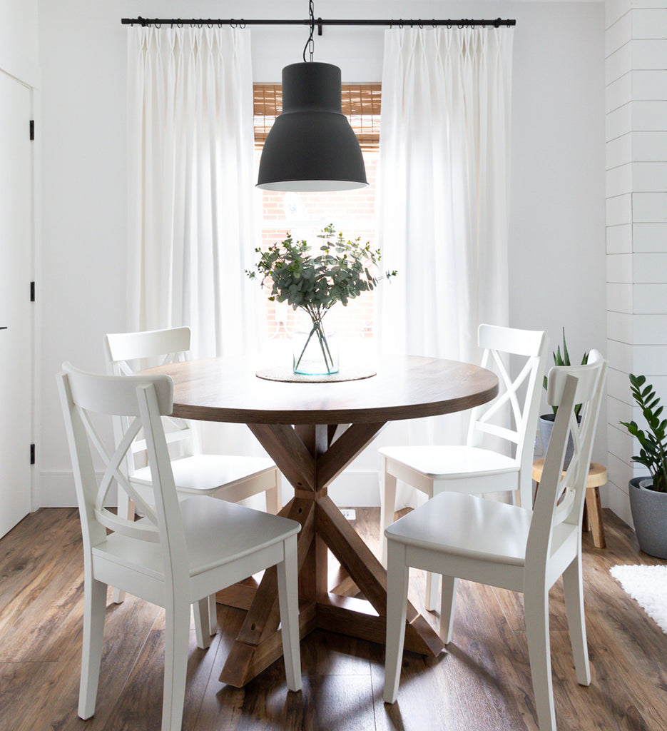 Round wood table with white chair with with off-white double pinch drapery panels in background