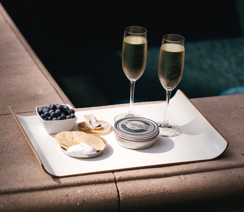 two glasses with champagne, one bowl with blueberries, two pearl spoons and a tin of Petrusco caviar