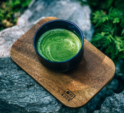 Photo of matcha green tea in a dark cup on a wooden board