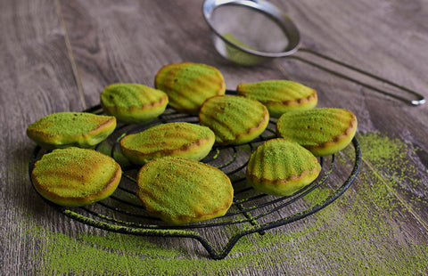 Photo of madeleine cookies dusted with green tea, with a small hand sifter in the background