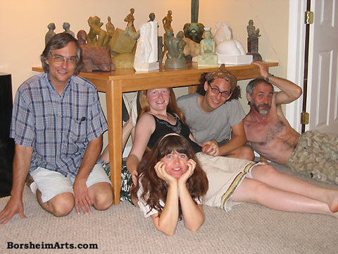 Sculptors and friends and Family pose under a table of small stone carvings statues sculptures