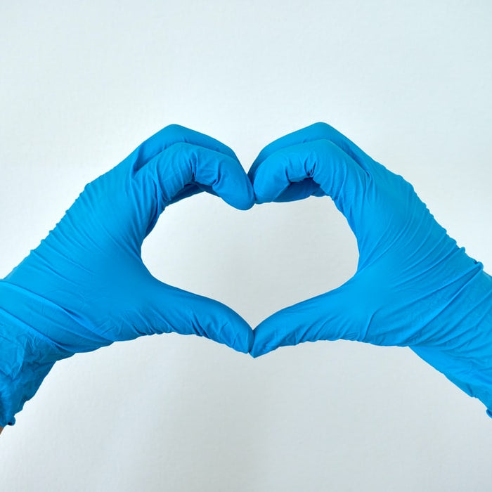 Hands wearing disposable gloves while forming a hand heart
