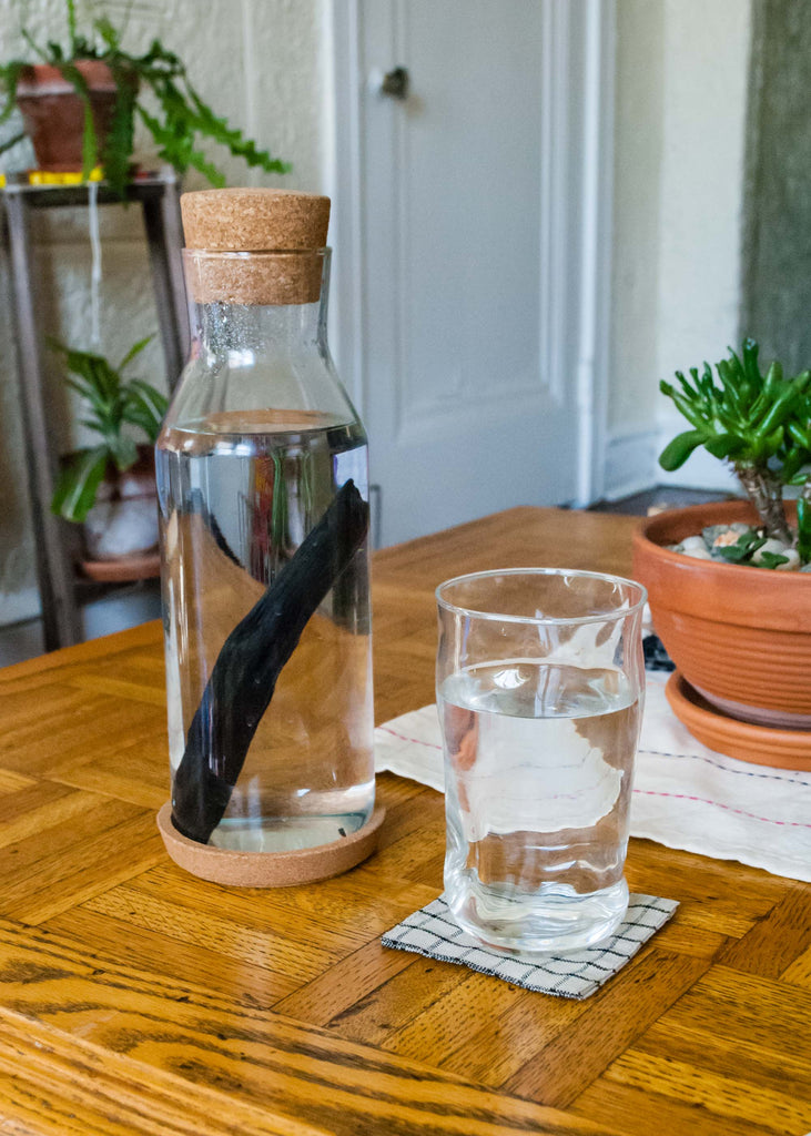 A water jug from IKEA sits next to one of our TebiNeri drinking glasses on a thrifted wood table.