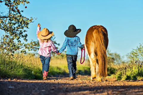 Two cowboy children and a pony walking a trail