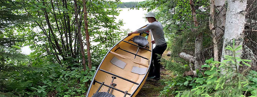 small person portaging a canoe