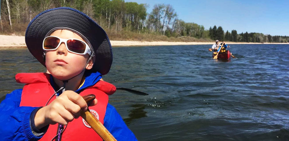 Child paddling canoe wearing sunglasses